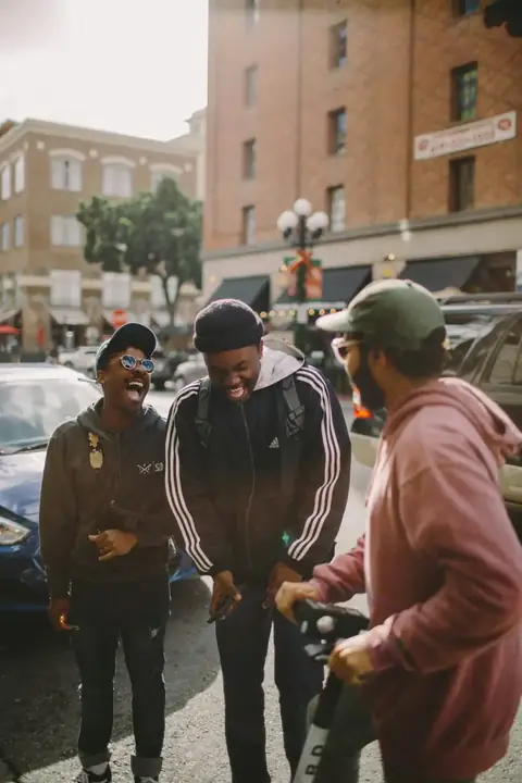 Three friends laughing together on a sunlit city street